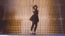 a woman in a black dress and black hat is dancing in front of a wall of lights