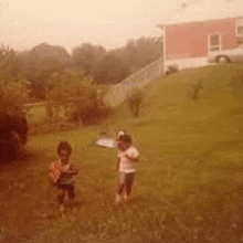 two children are standing in a grassy yard in front of a house .