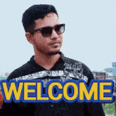 a man wearing sunglasses and a black shirt that says welcome