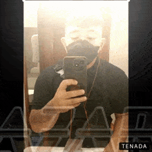 a man wearing a mask takes a selfie in front of a mirror with the word tenada below him