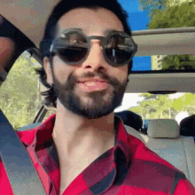 a man with a beard is wearing sunglasses and a red plaid shirt