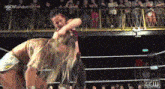 a woman is wrestling another woman in a wrestling ring while a crowd watches .