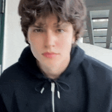 a young man in a black hoodie is looking at the camera .