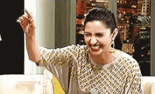 a woman is sitting on a couch making a funny face and raising her hand .