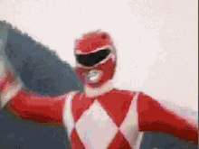 a red power ranger with his arms outstretched is flying through the air .