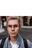 a man wearing glasses and a denim jacket is standing on a street .