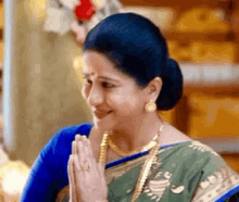 a woman in a blue and green saree is smiling with her hands folded .