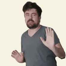 a man with a beard wearing a gray shirt waves his hand