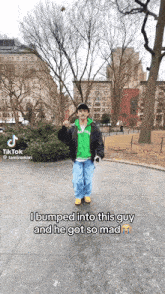 a man in a green hoodie and black jacket is standing in a park with trees in the background