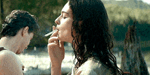 a woman is smoking a cigarette in front of a man .