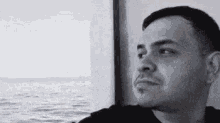 a man is looking out of a window at the ocean in a black and white photo .