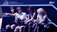 a group of girls are sitting in a row on a stage and dancing .