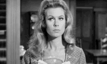 a black and white photo of a woman in a polka dot dress holding a glass bowl .