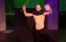 a man without a shirt is dancing with his arms outstretched in front of a green screen .
