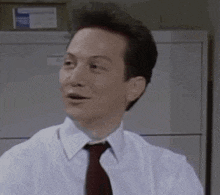 a man in a white shirt and red tie is sitting in an office .