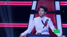 a woman in a white suit with a parrot embroidered on it is sitting in front of a screen .