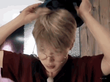a man wearing glasses and a red shirt is putting a hat in his hair .