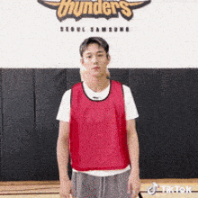 a man wearing a red vest is standing in front of a wall with the word thunders on it