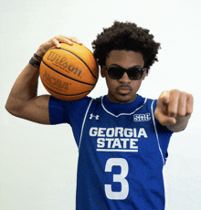 a man wearing a georgia state jersey holds a wilson basketball