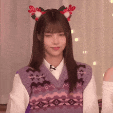 a woman wearing a sweater vest and a reindeer headband is making a funny face .