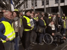 a man in a wheelchair is surrounded by people wearing yellow vests .
