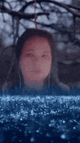 a woman wearing ear buds stands in the rain looking at something