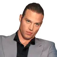 a man wearing a black shirt and a gray jacket looks at the camera