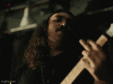 a man with long hair is playing a guitar in a dark room .