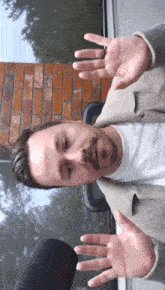 a man with his hands outstretched in front of a window with a brick wall behind him
