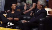 two men are sitting on a couch talking to each other with a man holding a microphone with the letter s on it