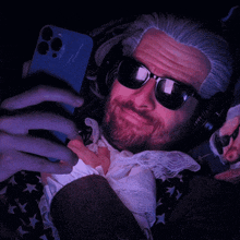 a man with a beard wearing sunglasses and headphones looks at his phone