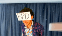 a man in a polka dot shirt is holding a sign over his face that says bpd