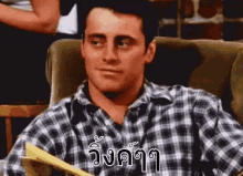 a man in a plaid shirt is sitting in a chair with a book in his hands .