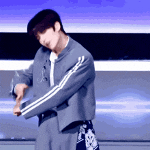 a man in a grey jacket with white stripes on the sleeves is dancing on a stage
