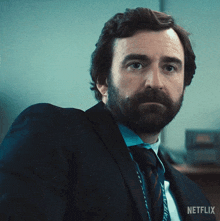 a man with a beard wearing a suit and tie with a netflix logo on his chest