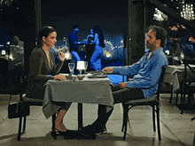 a man and a woman sit at a table in a restaurant with a woman dancing in the background