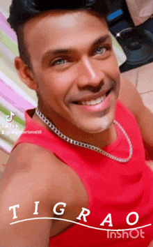 a man wearing a red tank top and a silver chain smiles