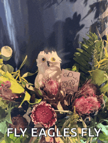 a white owl sitting in a bouquet of flowers with a sign that says go birds