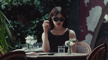a woman wearing sunglasses is smoking a cigarette at a table