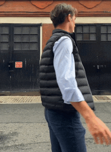 a man wearing a black vest is walking down a street