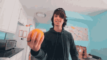 a man in a kitchen holds an orange in front of a map that says ' a ' on it