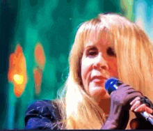a woman singing into a blue microphone with a green background