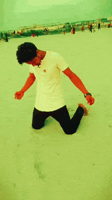 a man in a white shirt is kneeling down on the sand
