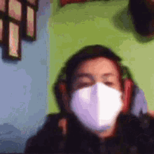 a man wearing a face mask and headphones is sitting in front of a green wall .