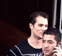 a man is talking on a cell phone while another man looks on .