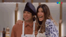 a man and a woman are posing for a picture in front of a masterchef argentina logo