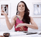 a woman in a pink top is sitting at a table with a magazine on the wall behind her that says ego