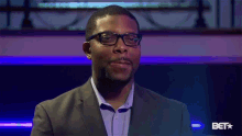 a man in a suit and glasses is standing in front of a bet sign .