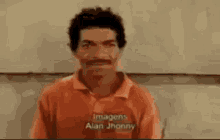 a man with a mustache is wearing an orange shirt and looking at the camera .