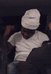 a man wearing a white hat and a white t-shirt is sitting in the back seat of a car .